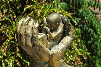 Skulptur, die ein Kleinkind in zwei Händen zeigt